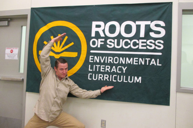 Travis Turley, Roots graduate and graduation speaker, poses in front of CRCC's Roots of Success sign after graduation.  Photo by Joslyn Rose Trivett 