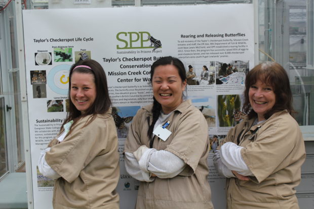 Butterfly technicians pose in front of educational poster set up for visiting Girl Scouts Behind Bars. 