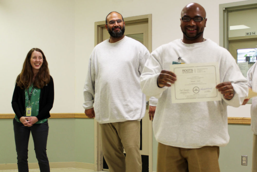A Roots of Success graduate shows his certificate while his instructor and SPP Co-Director celebrate his success at Monroe Correctional Complex. Photo by Erica Benoit.